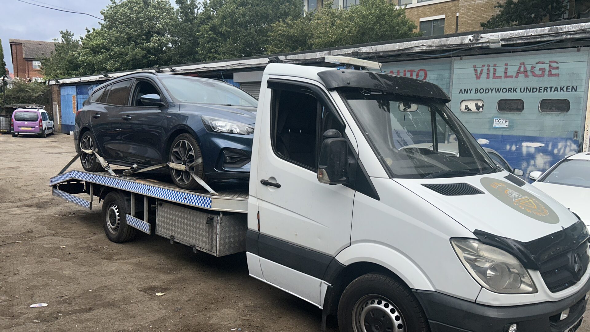 A white tow truck carrying a black car in an urban area.