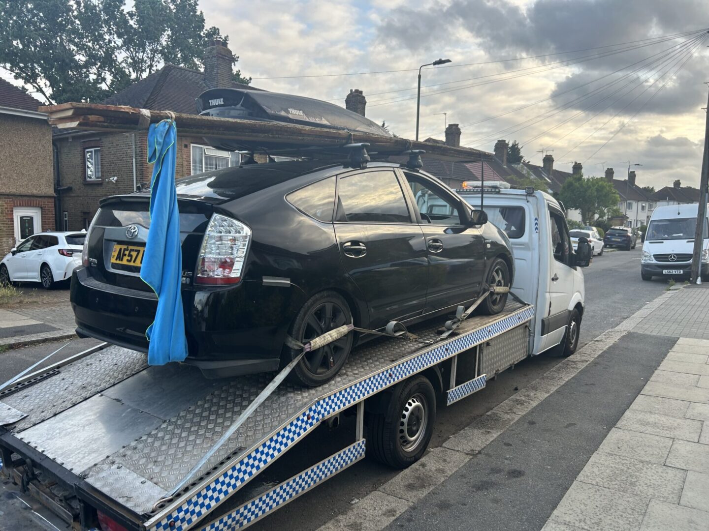 A black car loaded on a flatbed tow truck on a residential street.